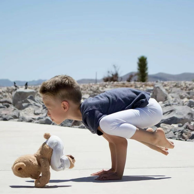 A young boy practicing the Crow Pose (Bakasana) in yoga alongside Meddy Teddy
